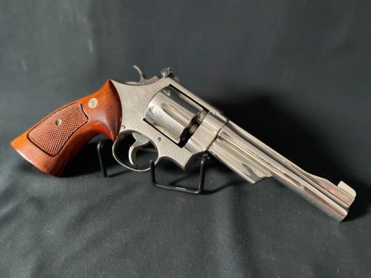 Smith and Wesson Model 27-2 .357 revolver with wood grips and polished nickel frame on a display stand with black background.