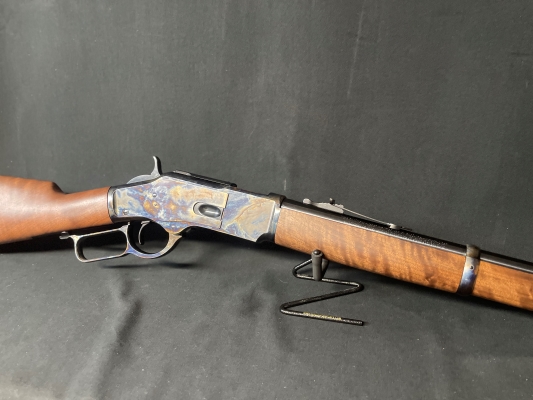 Mid section of a Winchester Model 1873 Competition Carbine facing to the right with a cold case hardened frame and wood stock/forend lever action rifle in .45 Long Colt on a display stand with a black background.