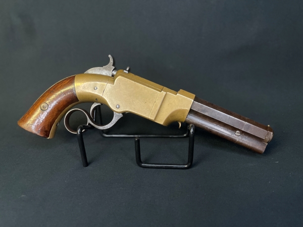 New Haven Arms Company No. 1 Volcanic lever action .31 caliber pistol with wood grips and brass receiver on a display stand facing to the right with a black background.