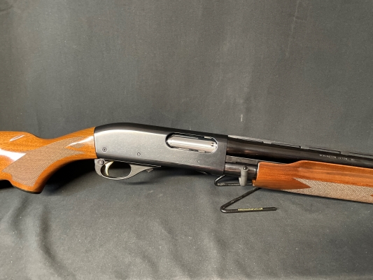 Mid-section of a Remington model 870 Wingmaster 12 gauge semi-action shotgun with wood stock/forend and black receiver and barrel facing to the right on a display stand with a black background.