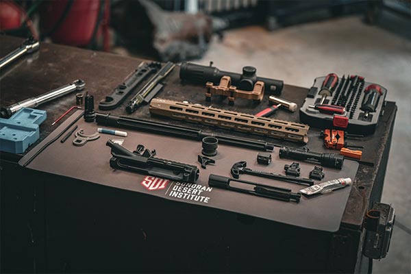 Disassembled AR-style rifle parts laid out on a Sonoran Desert Institute work mat in a gunsmithing workshop.
