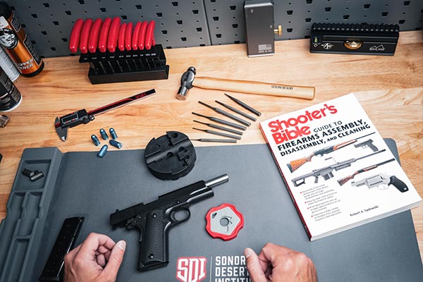 Disassembled handgun, tools, and a copy of the Shooter’s Bible laid out on a Sonoran Desert Institute workbench during firearm maintenance training.