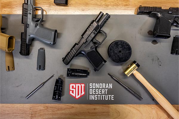 Handgun components, tools, and a rubber mallet arranged on a Sonoran Desert Institute workbench mat during firearms technology training.