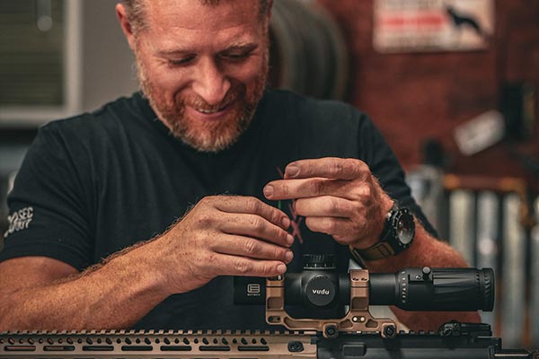 Smiling man mounting a Vudu rifle scope on an AR-platform rifle during firearms training.