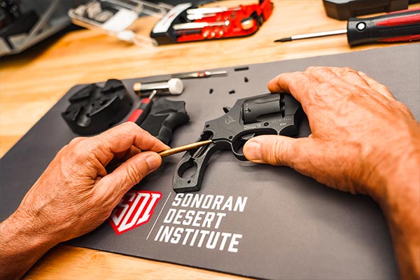Hands working on the trigger mechanism of a Taurus revolver on a Sonoran Desert Institute bench mat during gunsmithing training.